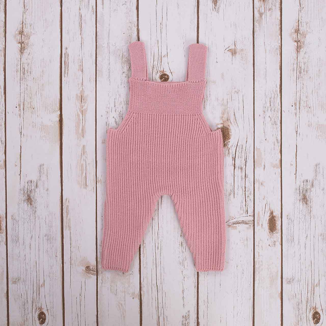 pink irish baby knitted romper overalls on a wooden background