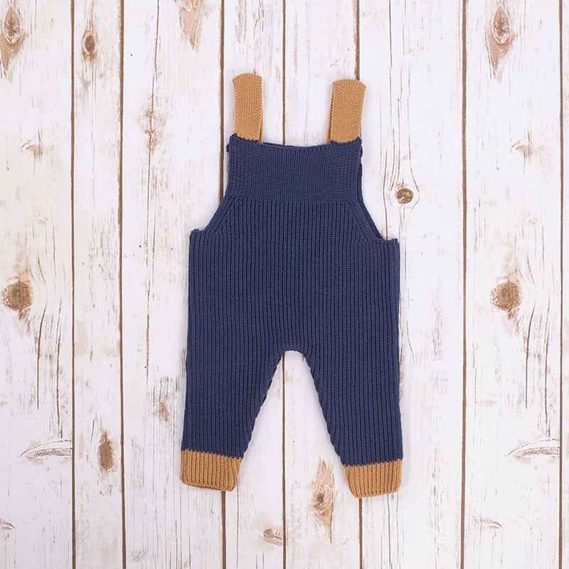 Reverse view of Navy blue Irish baby knitted romper overalls with brown cuffs and buttons on a wooden background