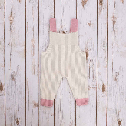Reverse view of White Irish baby knitted romper overalls with pink cuffs and buttons on a wooden background