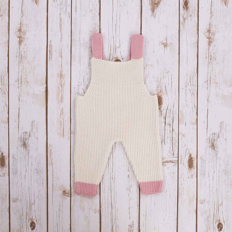 Reverse view of White Irish baby knitted romper overalls with pink cuffs and buttons on a wooden background