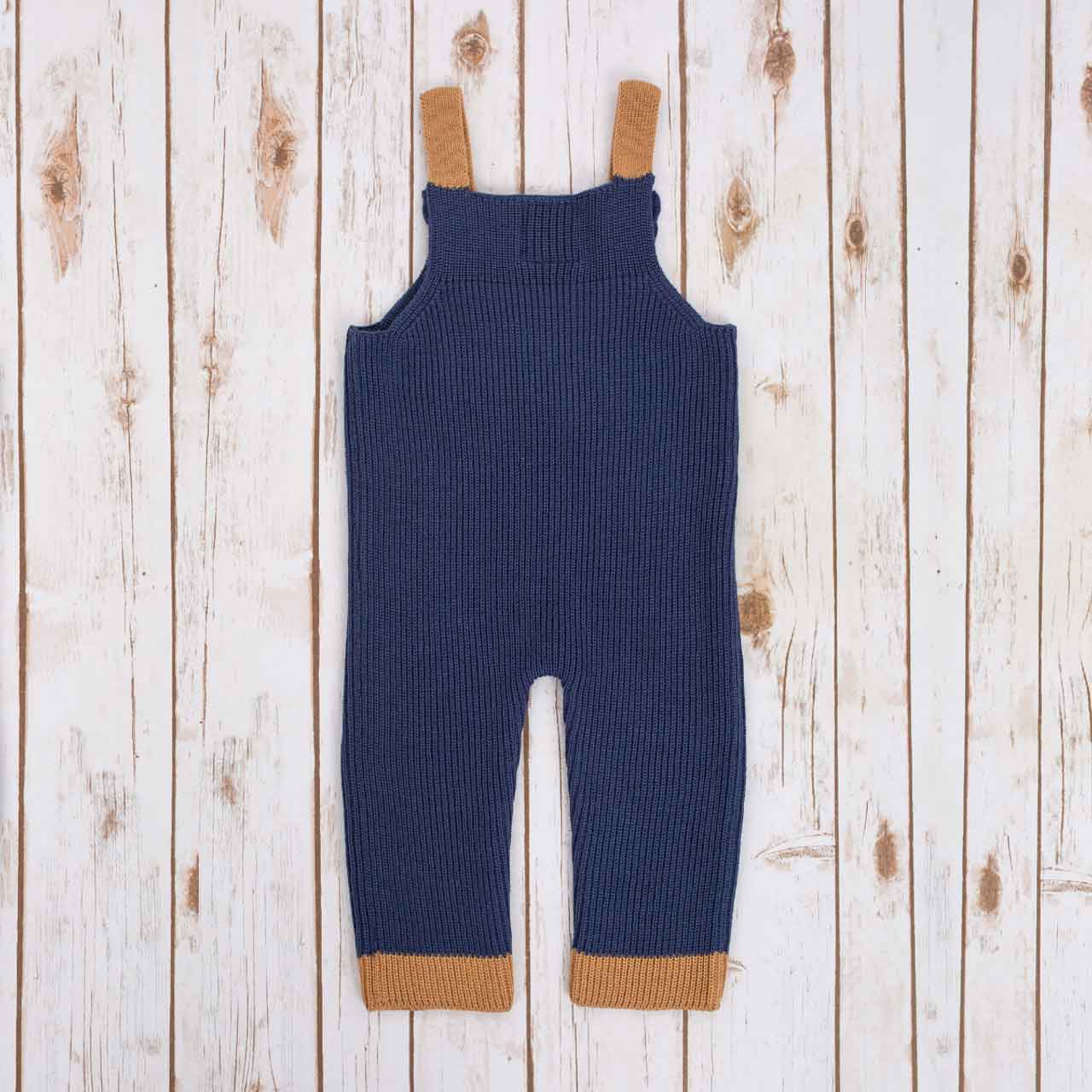reverse view of navy blue irish baby knitted romper with  brown cuffs, on a wooden background