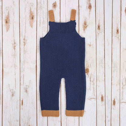 Reverse view of Navy Blue Irish baby knitted romper with  brown cuffs, on a wooden background
