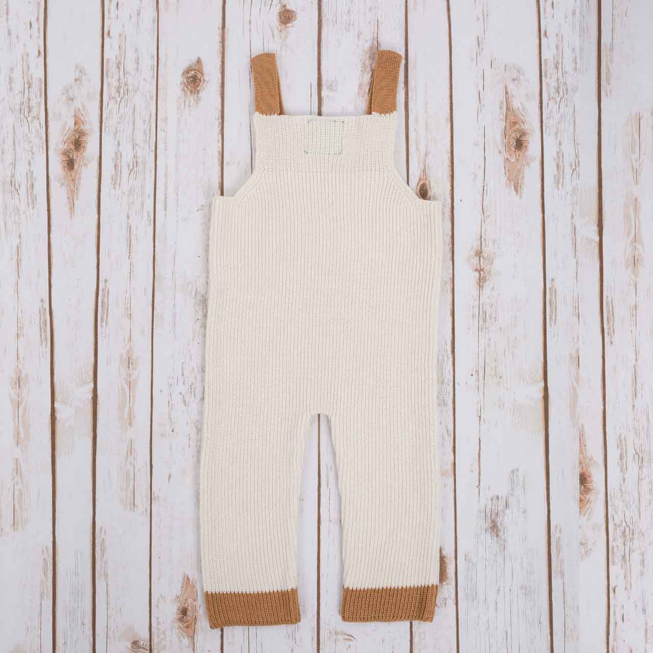 reverse view of white irish baby knitted romper with  brown cuffs, on a wooden background