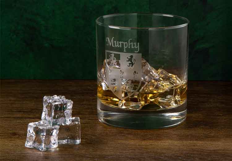 Irish Whiskey Tumbler etched with Murphy family Coat of Arms  and ice cubes on a wooden surface with a green background