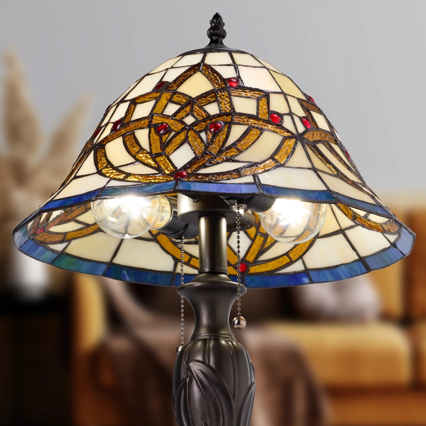 a celtic blooming flower tiffany-style stained glass table lamp with a conical shade featuring an interlaced geometric pattern in gold, blue, and cream glass, with two glowing bulbs and a dark metal base.