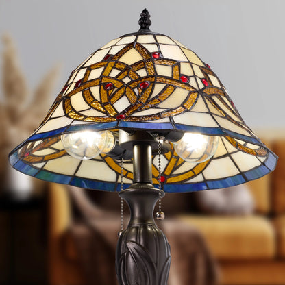 A Celtic Blooming Flower Tiffany-style stained glass table lamp with a conical shade featuring an interlaced geometric pattern in gold, blue, and cream glass, with two glowing bulbs and a dark metal base.