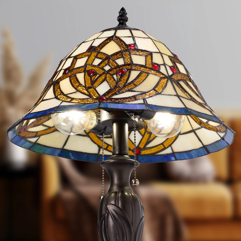 A Celtic Blooming Flower Tiffany-style stained glass table lamp with a conical shade featuring an interlaced geometric pattern in gold, blue, and cream glass, with two glowing bulbs and a dark metal base.