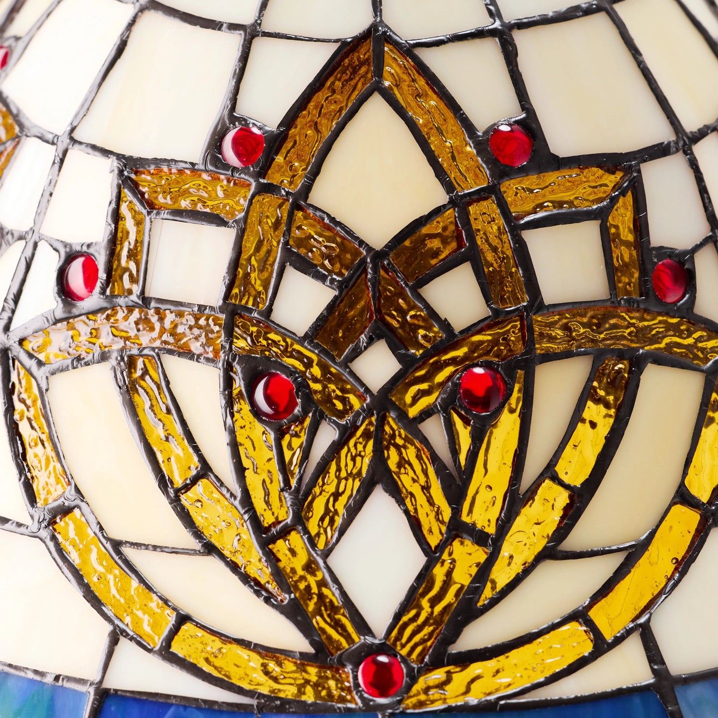 close-up of a celtic blooming flower stained glass table lamp featuring a central interlaced geometric motif in gold and amber tones, bordered by cream glass sections and accented with small red glass gems.