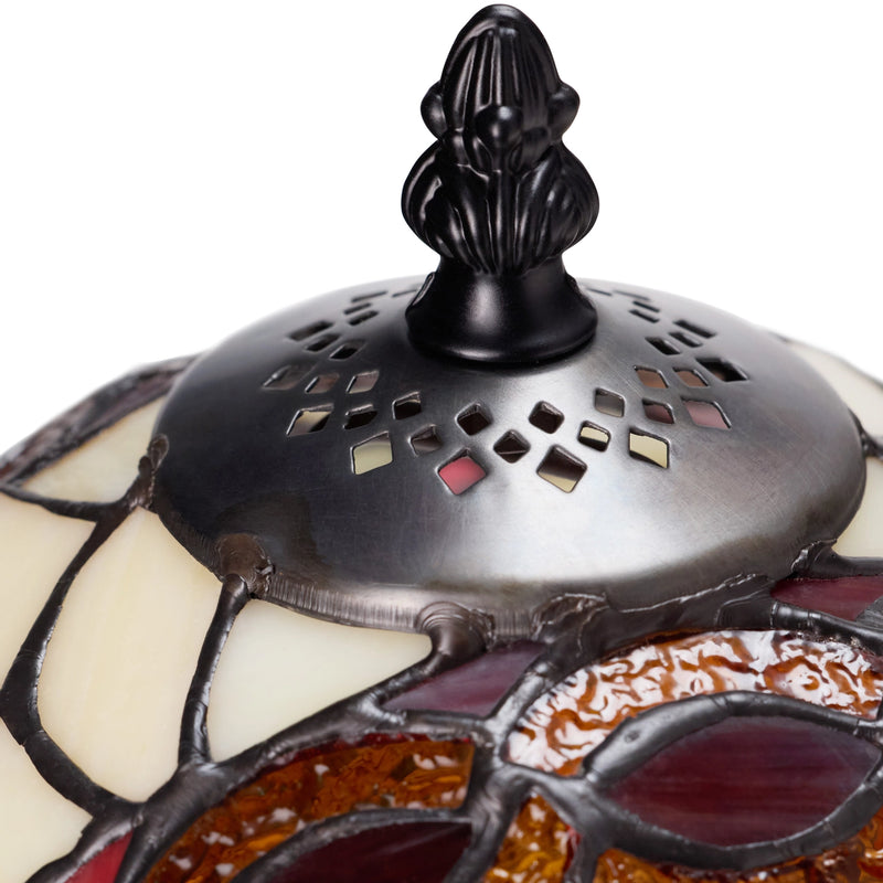 Close-up detail of a Claddagh Stained Glass Table Lamp shade, showing cream, amber, and burgundy glass panels with a dark metal perforated cap and black finial on a white background.