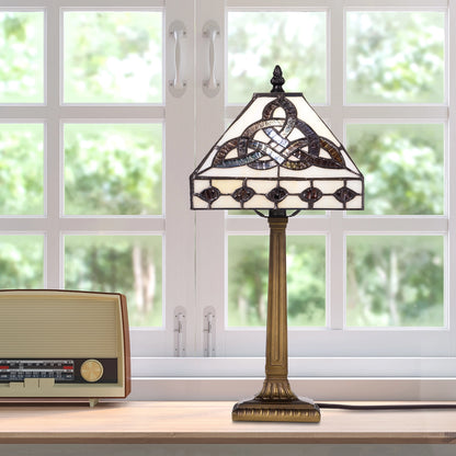 A vintage-style Celtic Trinity Knot Stained Glass Table Lamp featuring a Celtic knot design and a bronze-toned column base, set on a windowsill next to a retro radio.