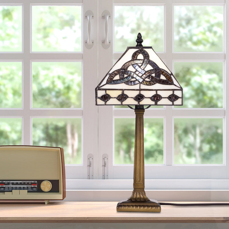 A vintage-style Celtic Trinity Knot Stained Glass Table Lamp featuring a Celtic knot design and a bronze-toned column base, set on a windowsill next to a retro radio.