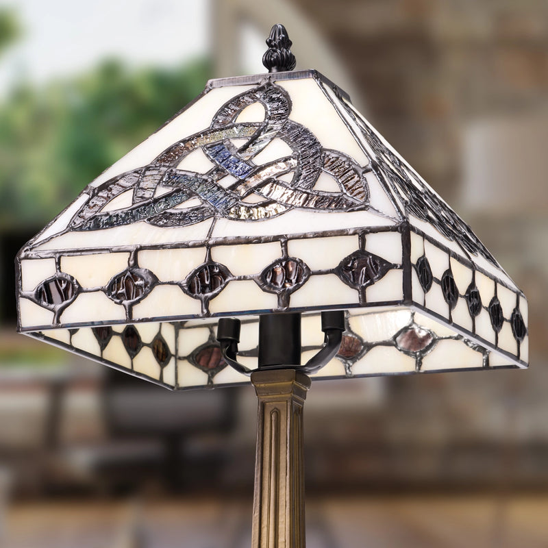 A stained glass table lamp with Celtic Trinity Knot shade featuring cream glass panels and dark metal accents, mounted on a bronze-colored stand.