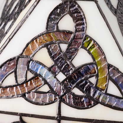 Close-up of a Celtic Trinity Knot Stained Glass Table Lamp featuring a Celtic triquetra knot design with iridescent segments in purple, blue, green, and brown, held together by dark metal solder over a cream glass background.