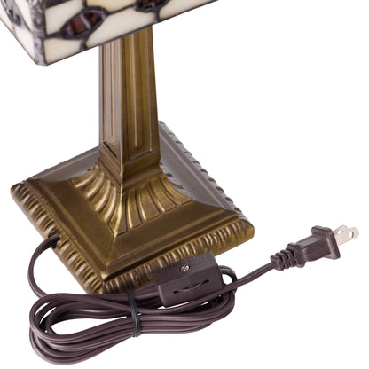 A close-up of a table lamp's base and power cord on a white background. The lamp has a square, ornate bronze-colored base and a stained-glass shade with cream, black, and brown mosaic patterns.