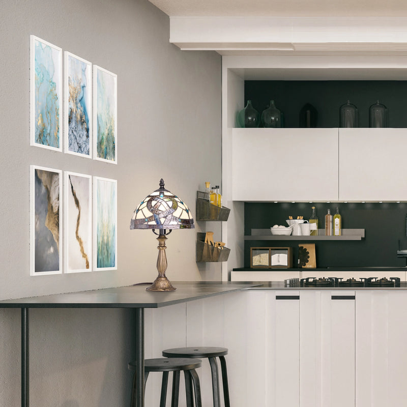 A modern kitchen interior with a bar-height counter, black stools, wall-mounted framed abstract art, Celtic Stained Glass Amber Pathway Table Lamp on the counter.