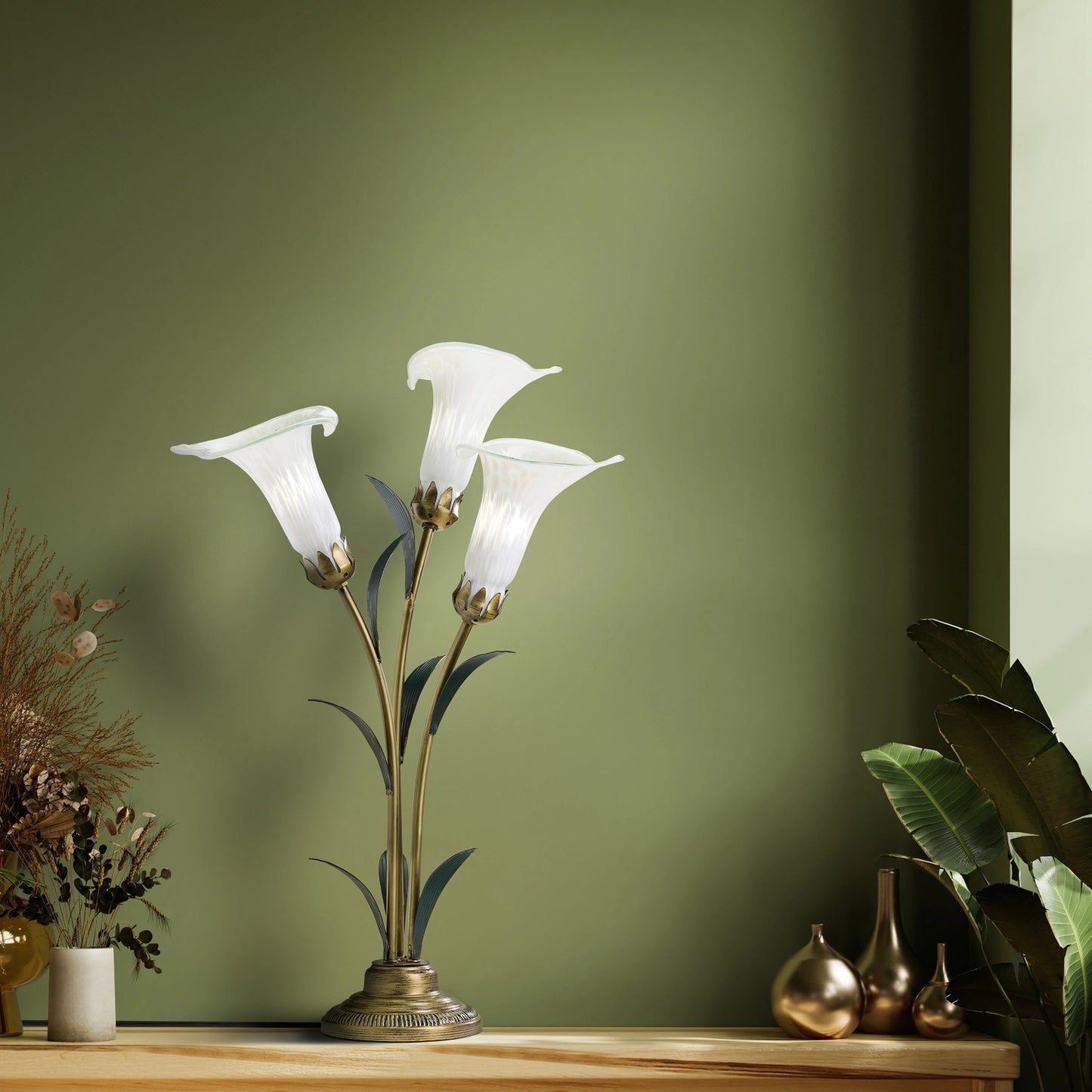 handblown glass 3 light white lily table lamp on a wooden surface against a green wall.