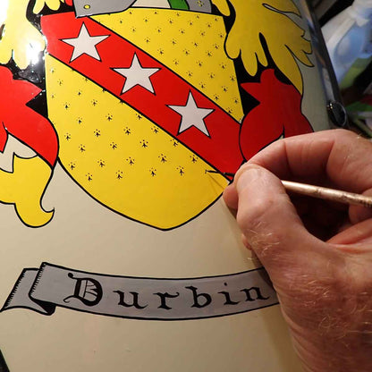 Close up of heraldic artist hand painting a family crest in yellow and red with the name 'Durbin'