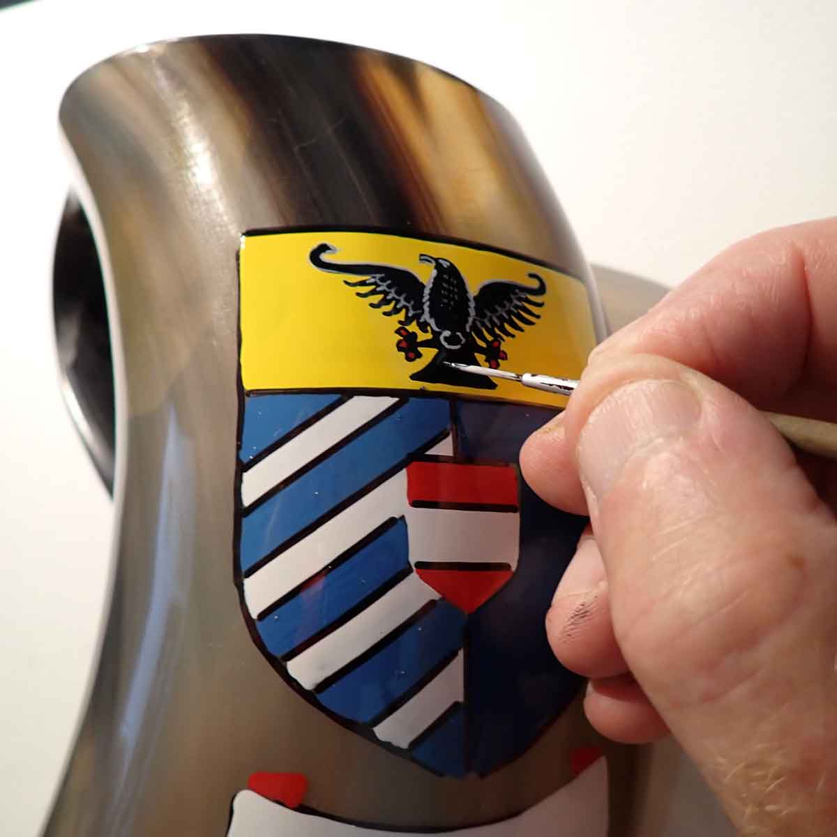 close-up of a heraldic artist hand painting a viking horn tankard