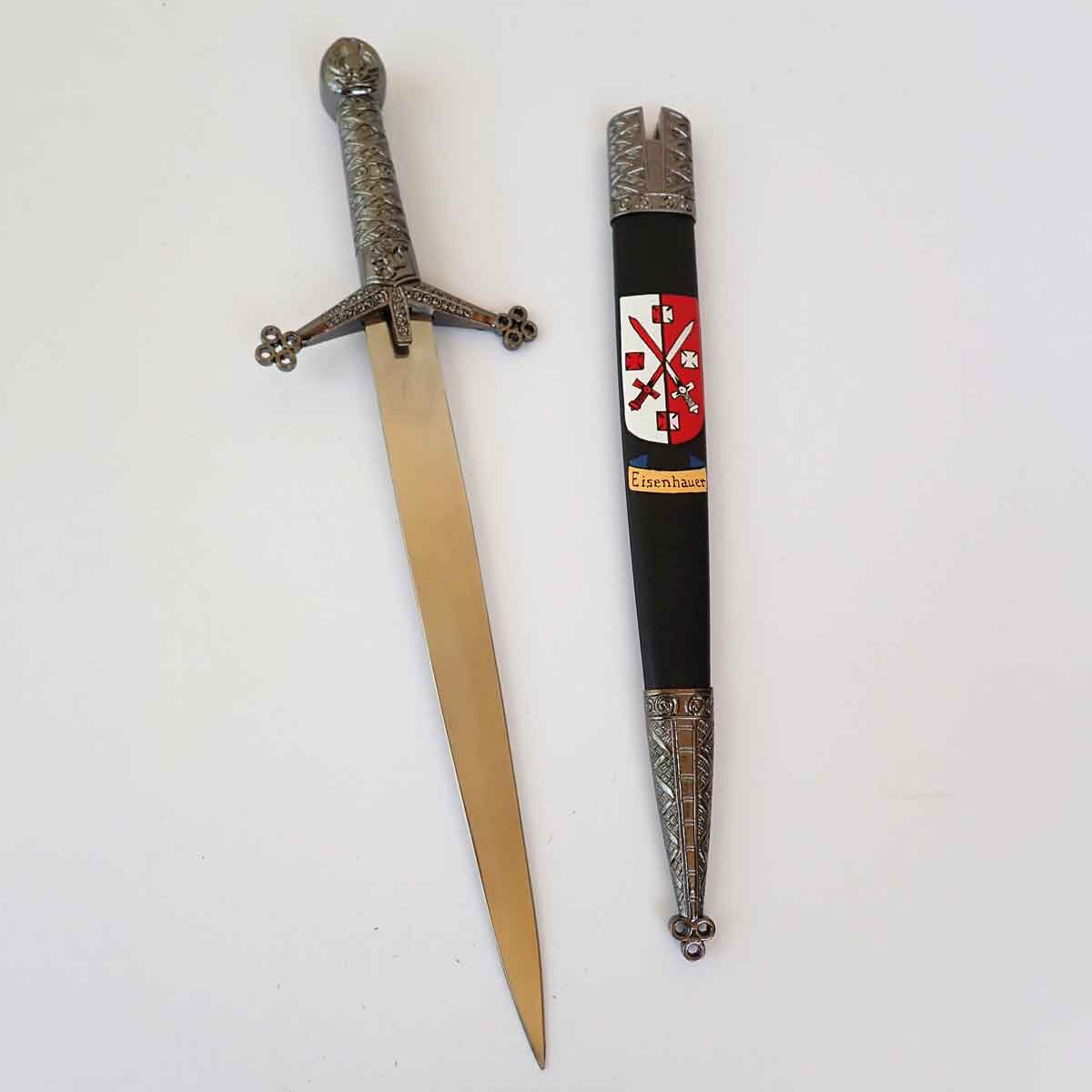 claymore dagger with ornate hilt beside a sheath decorated with a hand painted coat of arms on a white surface