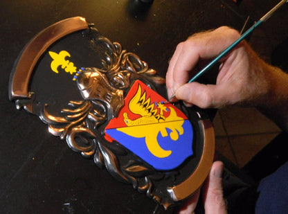 A closeup of our heraldic artist painting a Coat of Arms in vivid colors on a copper plaque
