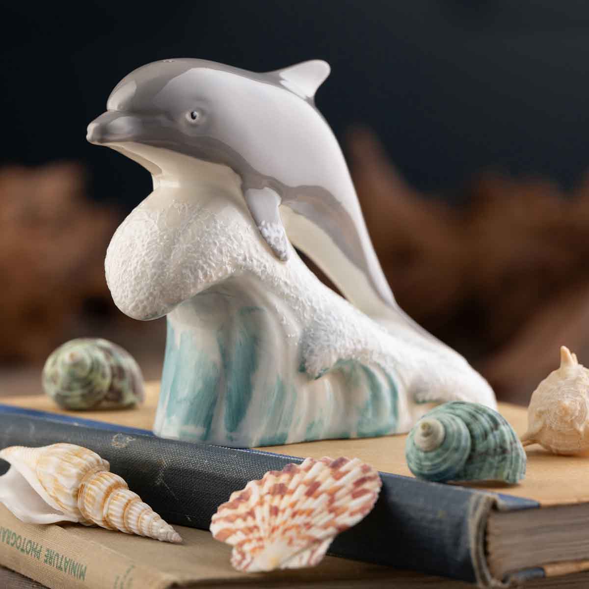 belleek pottery dolphin on a wave figurine on a blurred background with seashells & books