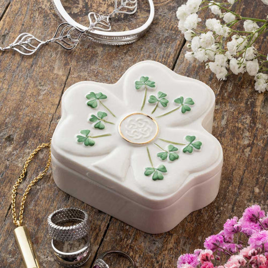 Belleek Pottery Irish Shamrock Shaped Trinket Box on a wooden surface with flowers and jewelry around.