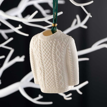 Belleek Pottery Aran Jumper Christmas Ornament, on a green ribbon, hanging on a white tree against a black background.