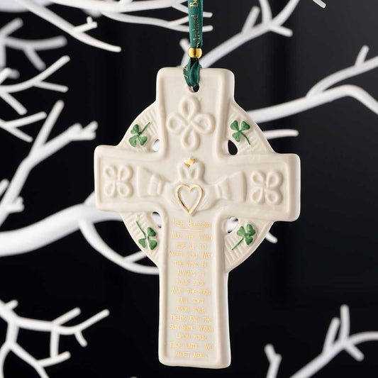 Belleek Pottery Claddagh Blessing Cross Ornament hanging from a green ribbon on a white tree against a black background