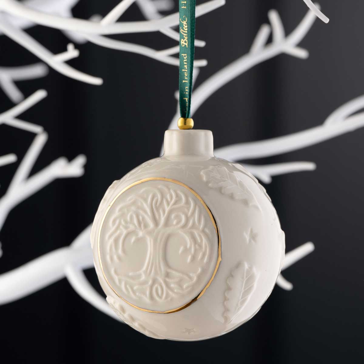 belleek pottery celtic tree of life bauble hanging from a green ribbon on a white tree against a black background