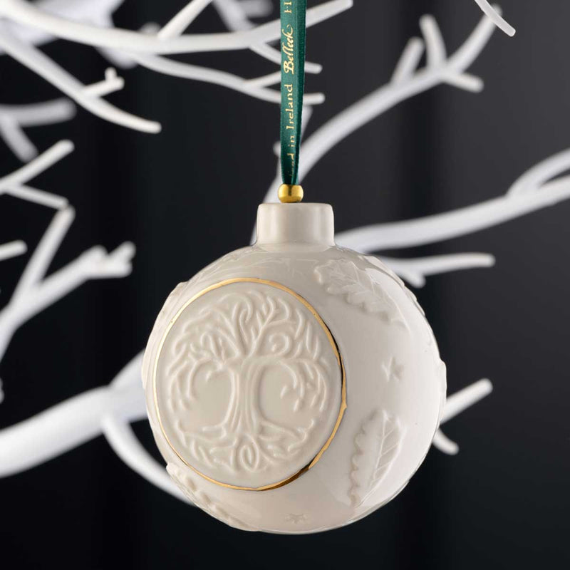 Belleek Pottery Celtic Tree of Life Bauble hanging from a green ribbon on a white tree against a black background