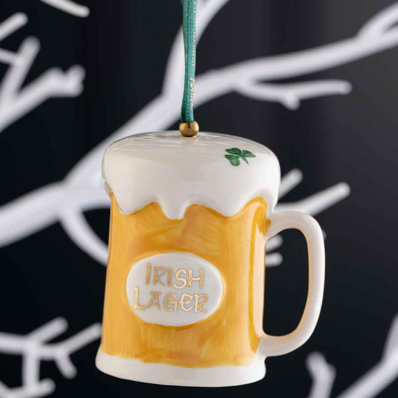 Irish Christmas | Belleek Pottery Beer Hanging Ornament hanging by a green ribbon against a black background with white tree branches.
