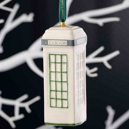 Irish Christmas Belleek Pottery Traditional Irish Telephone (Telefón) Box Ornament with green accents and a dark green hanging ribbon, shown against a dark background with white branch silhouettes.