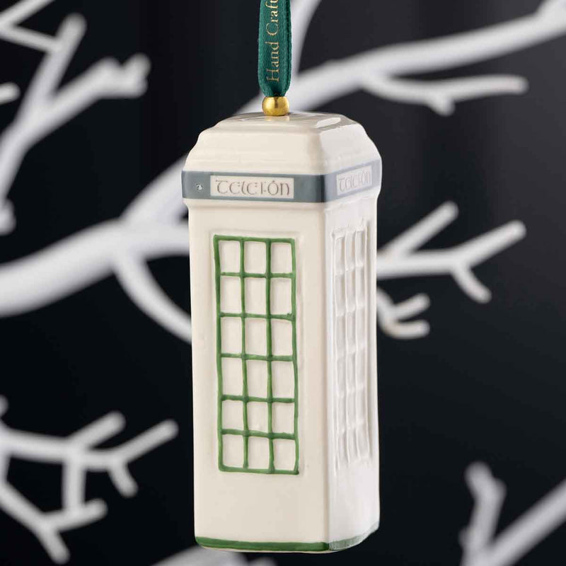 Irish Christmas Belleek Pottery Traditional Irish Telephone (Telefón) Box Ornament with green accents and a dark green hanging ribbon, shown against a dark background with white branch silhouettes.