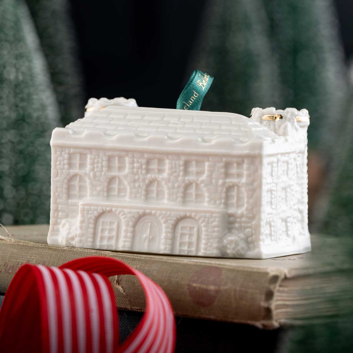reverse view of the kilkenny castle belleek pottery annual irish christmas ornament 2026 with a green ribbon on on a surface with a blurred green background.