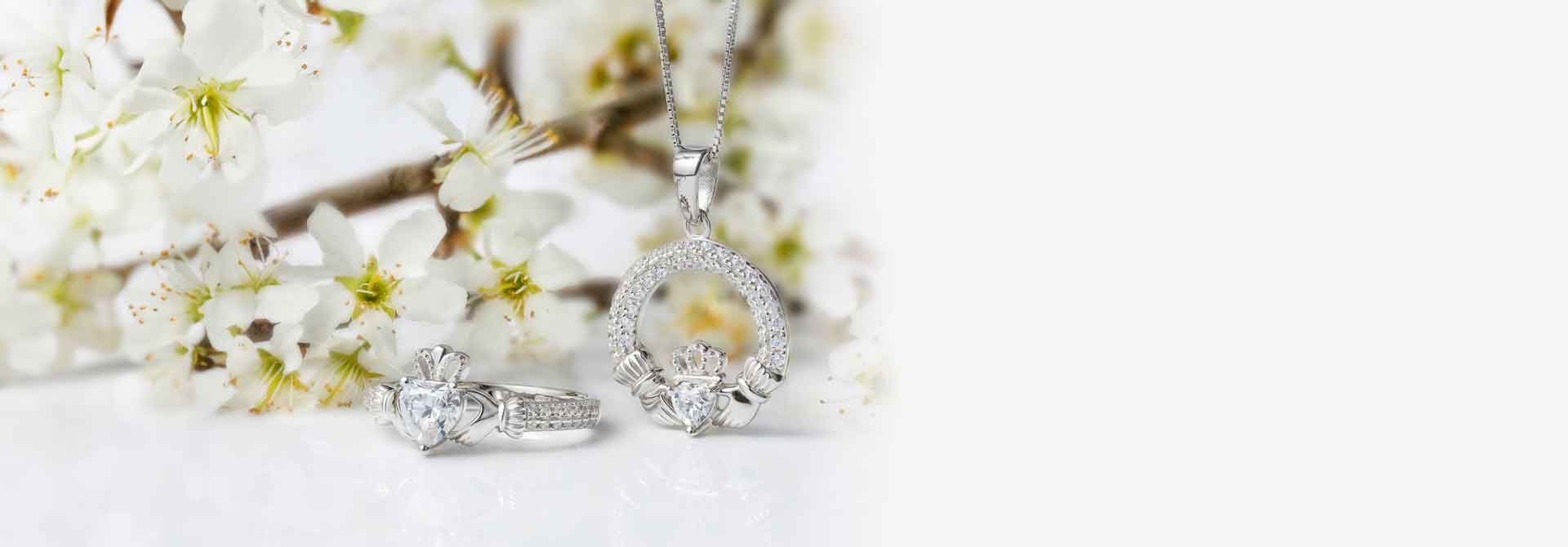 Silver Claddagh Ring and Necklace set with crystal hearts. In front of a background of white flowers