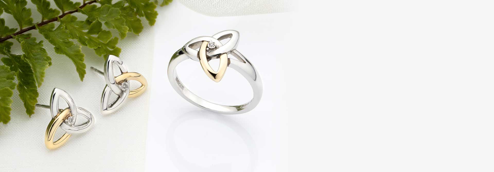 Silver & Gold Earrings and Ring with a trinity knot design on a white background with green leaves.