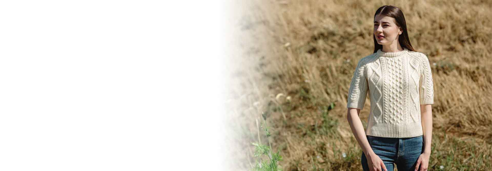 Woman wearing a Ladies Cable Knit Short Sleeve Aran Sweater, in color Natural,  standing in a field