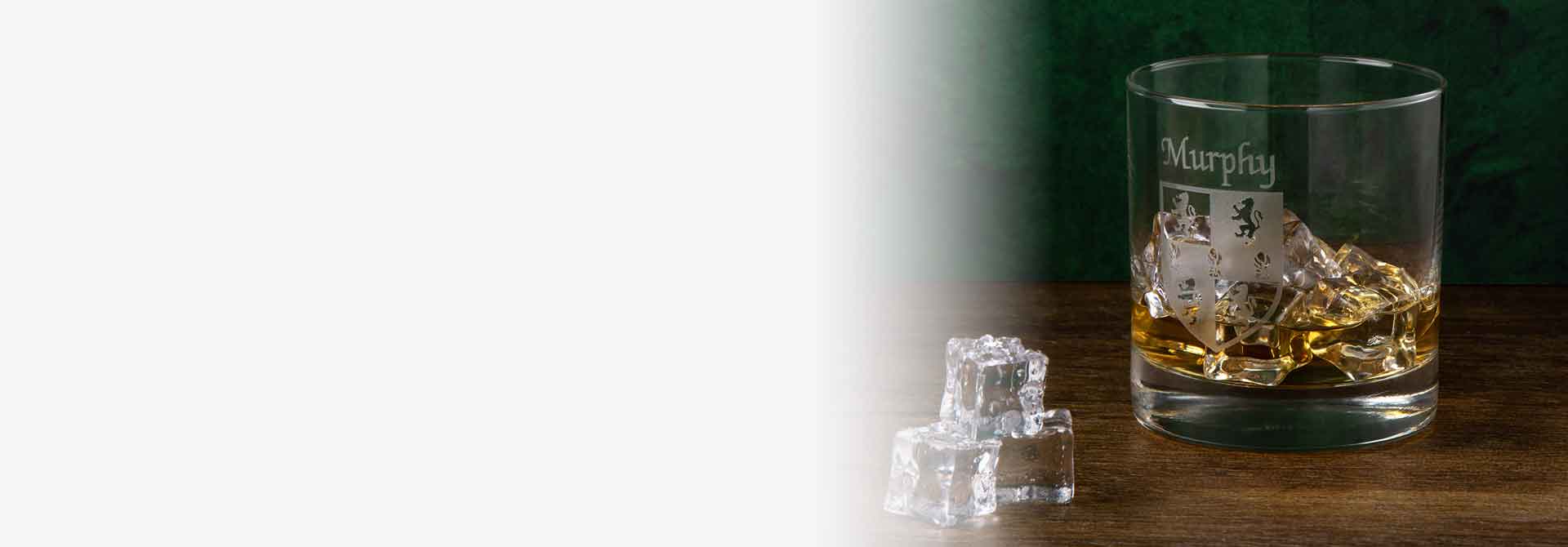 Irish Whiskey Tumbler etched with Murphy family Coat of Arms  and ice cubes on a wooden surface with a green background