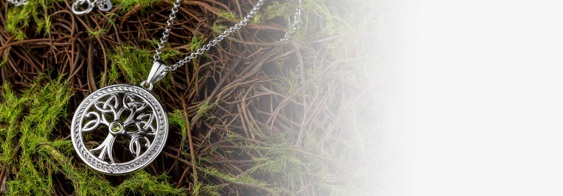 A Sterling Silver Celtic Trinity Knot Necklace with Green crystal at its center on a bed of green moss
