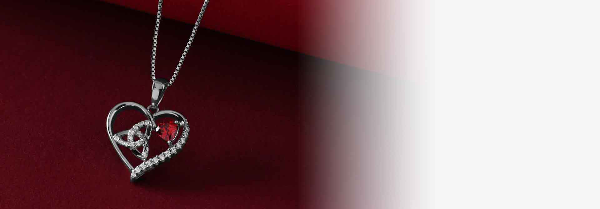 Heart-shaped Sterling Silver Irish Trinity Knot Necklace with a red gemstone on a dark red background