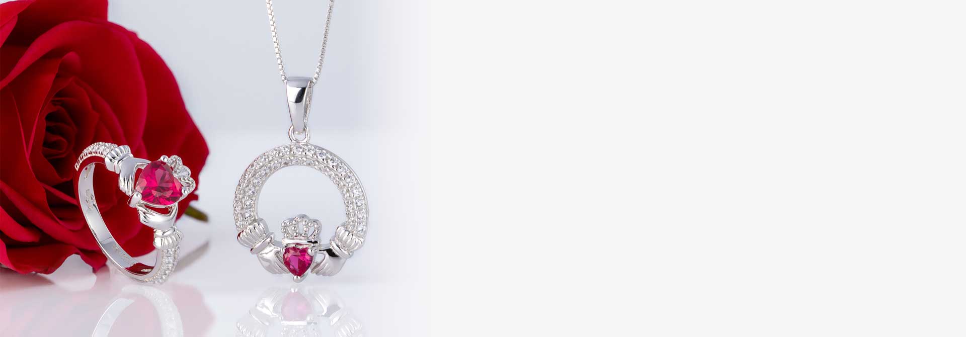 A Sterling Silver Claddagh Ring and Necklace Set with Ruby crystal birthstone on a grey surface with a red rose