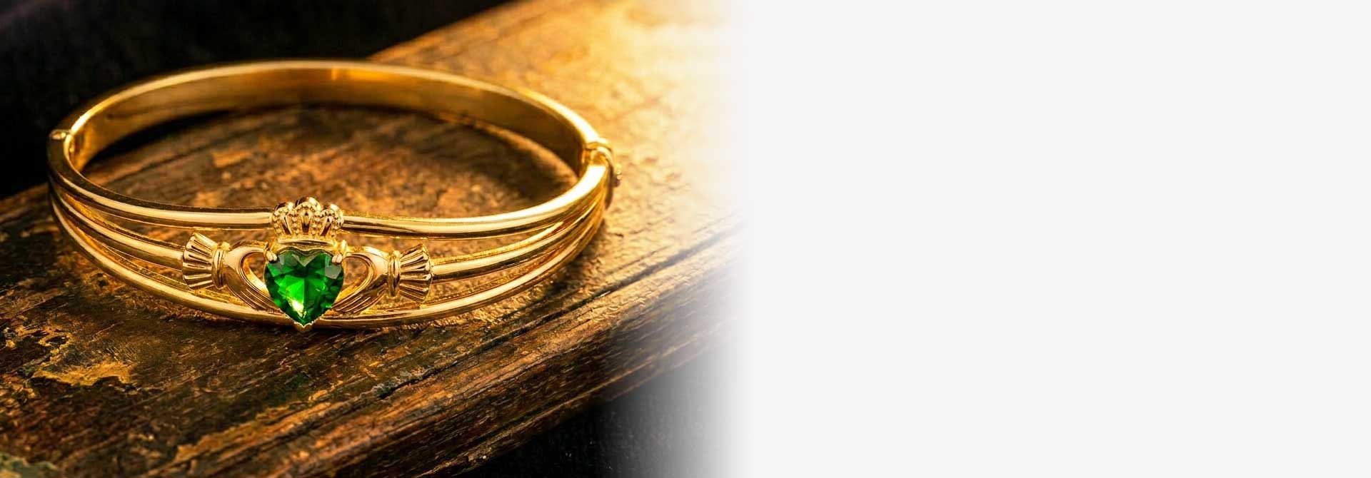 Gold Plated Green Crystal Heart Claddagh Bangle on a wooden surface