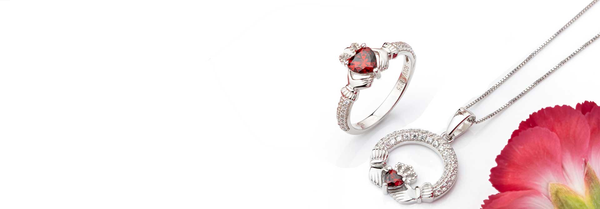 Sterling Silver Claddagh Ring and Necklace with Garnet birthstones in the heart beside a red flower on a white background