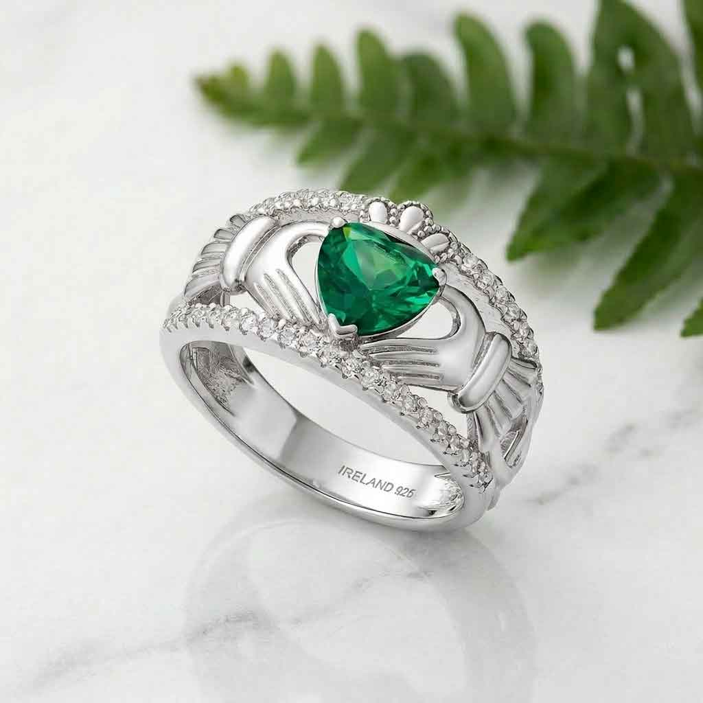 sterling silver celtic band with green crystal claddagh ring on a marble surface with fern leaves in the background