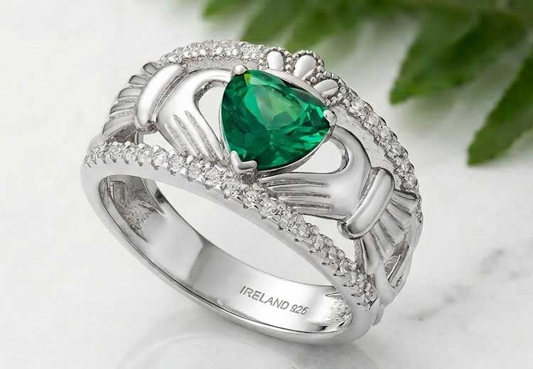 Sterling Silver Celtic Band with Green Crystal Claddagh Ring on a marble surface with green leaves in the background