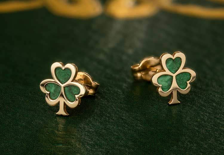 Close up of a pair of 10k Gold Malachite Shamrock Stud Earrings on a dark green surface