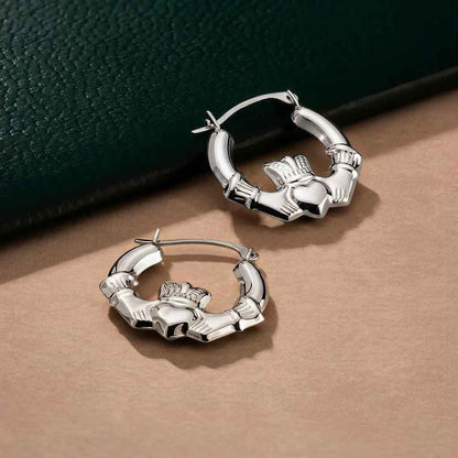 Sterling Silver Medium Hoop Claddagh Earrings on a beige surface