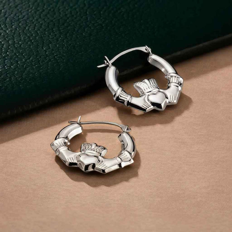 Sterling Silver Medium Hoop Claddagh Earrings on a beige surface