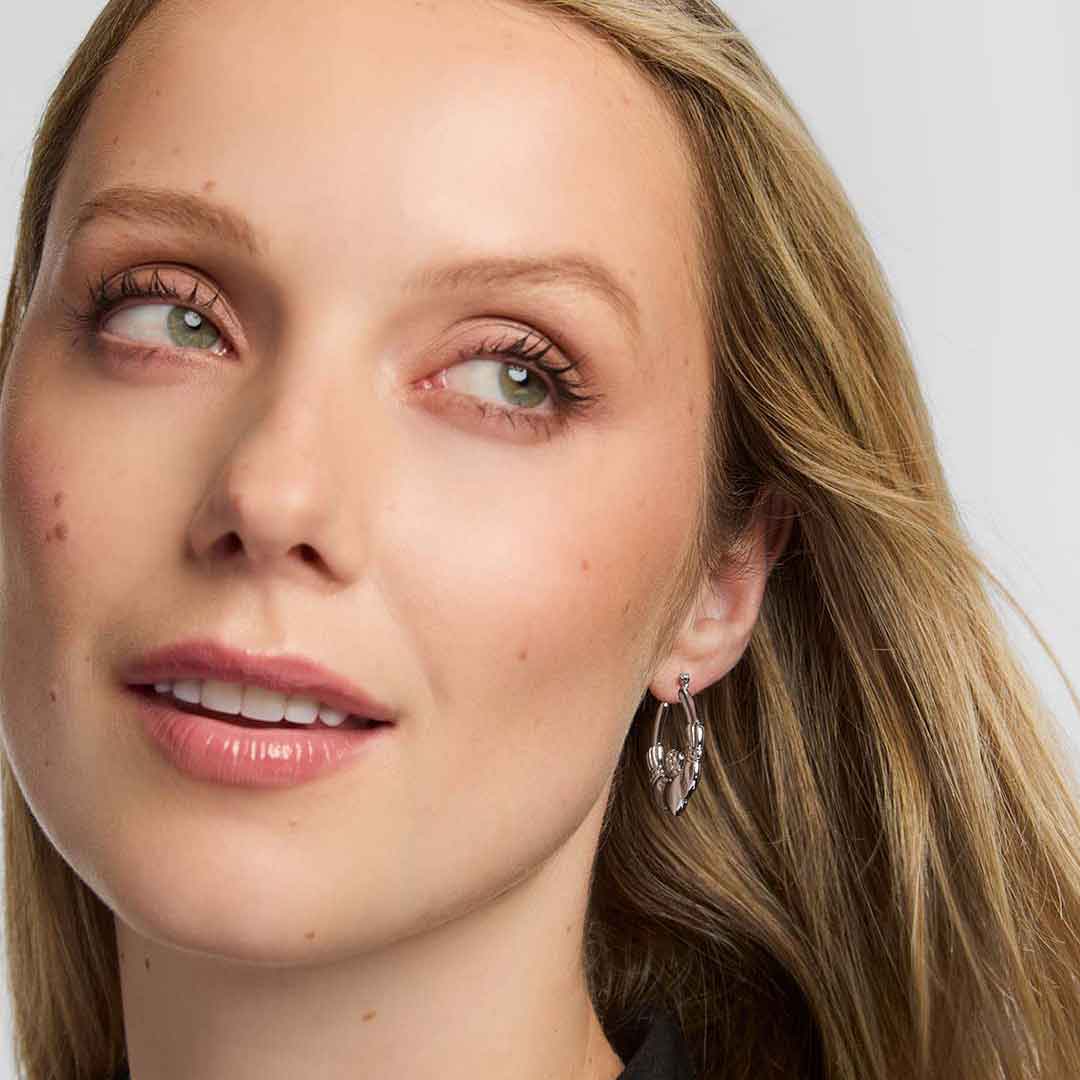 close-up of a woman wearing sterling silver medium hoop claddagh earrings with a plain background