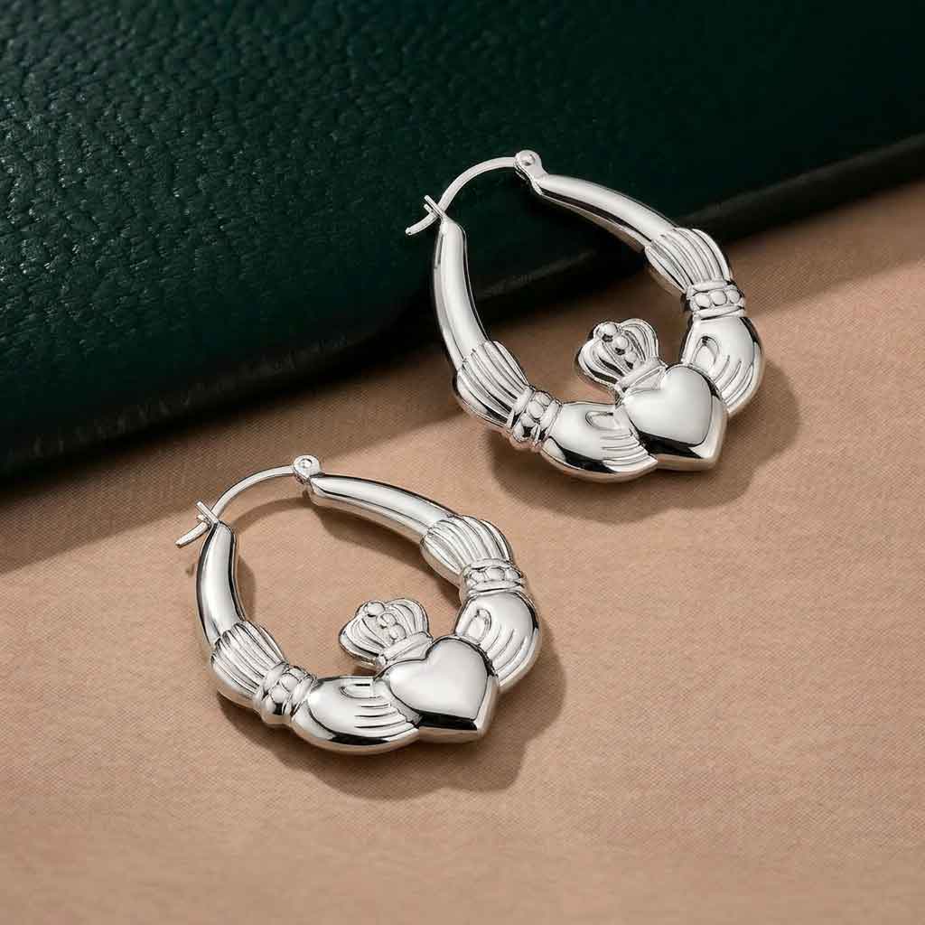 sterling silver large hoop claddagh earrings on a beige surface with a dark green background